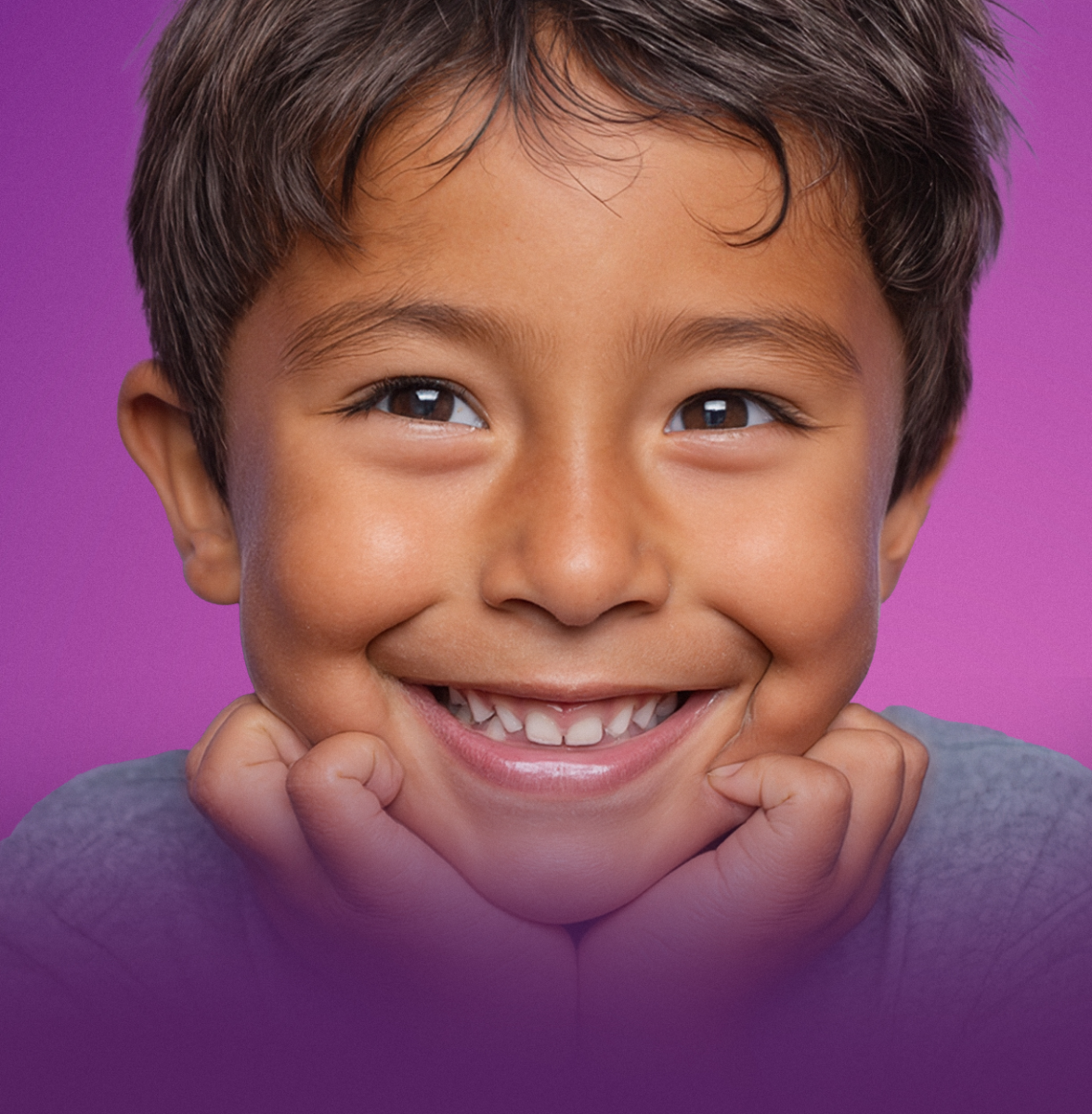A young boy smiling with his hands under his chin.